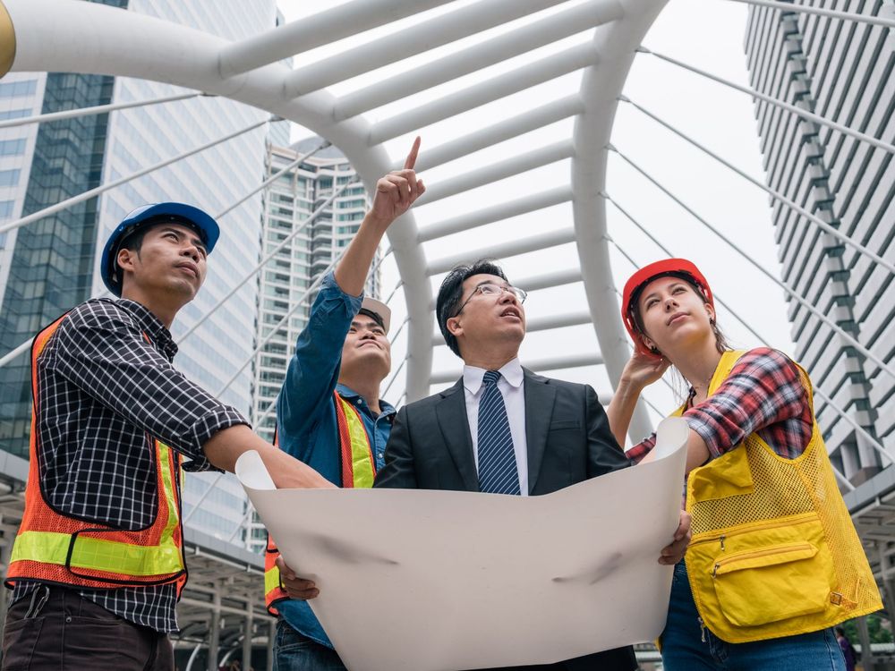 Giám đốc dự án cùng các kỹ sư xem bản vẽ tại công trình giữa các tòa nhà cao tầng